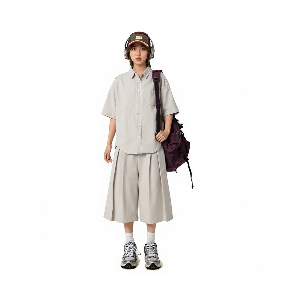 Model wearing an off-white short-sleeve button-up shirt with matching wide-leg shorts and a purple backpack
