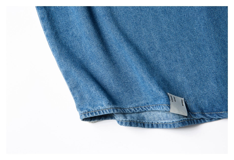 Close-up of a blue denim shirt hem with tan stitching and a small sewn-in label.