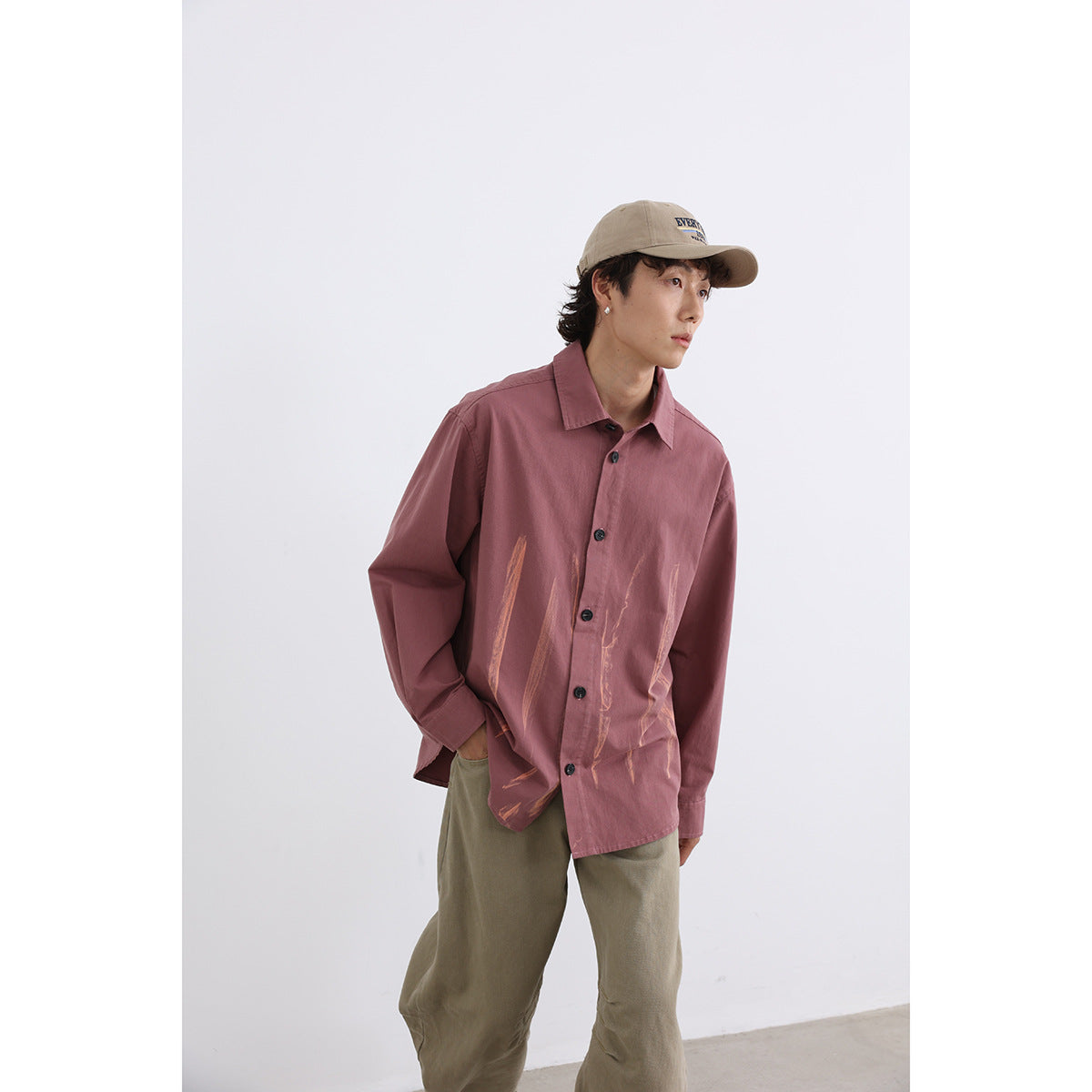 Model wearing a dusty rose button-up shirt with abstract peach brushstroke graphics.