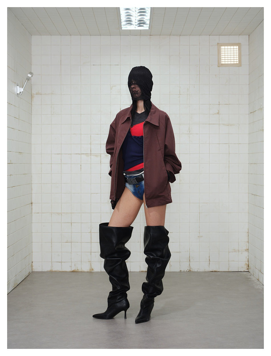 Front view of a model wearing an open burgundy collared jacket over layered tops, denim shorts, and tall black boots.