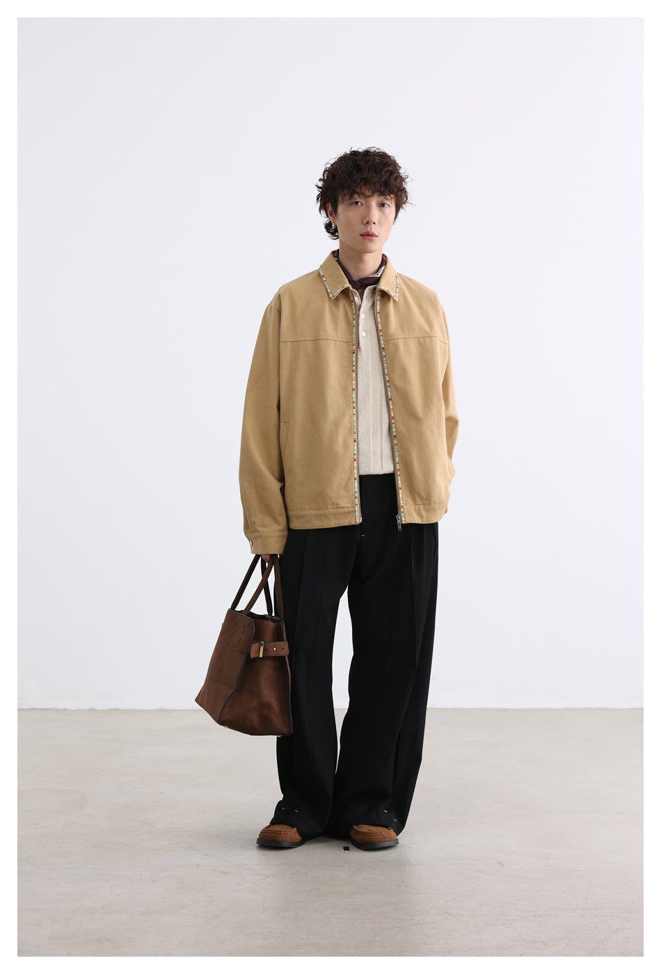 Full-length front view of a model wearing a tan zip-front jacket with multicolor trim and black wide-leg trousers.