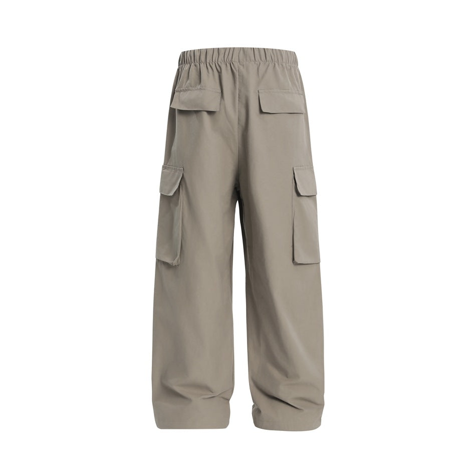Back view of loose taupe cargo pants with an elastic waist, two rear flap pockets, and large side cargo pockets.