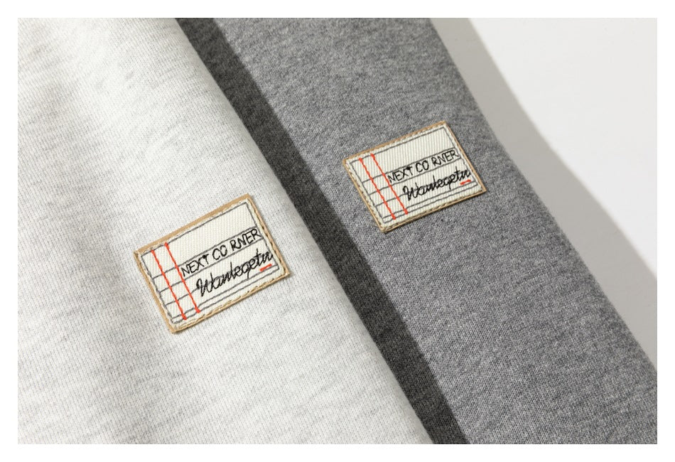 Close-up of off-white and gray fabric panels, each with a stitched rectangular patch bearing English text.