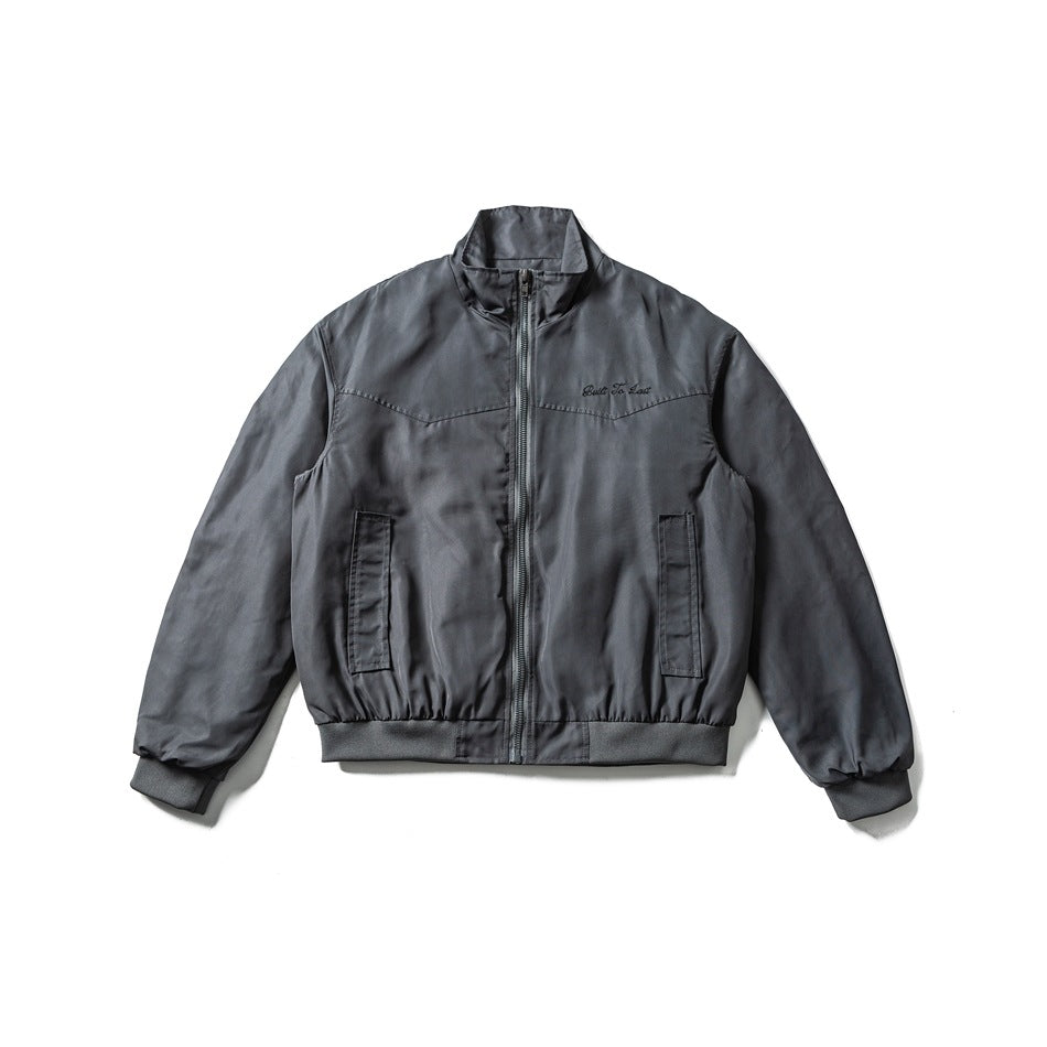 Blue-gray bomber-style zip jacket flat lay with chest yoke seam, script embroidery and ribbed trim