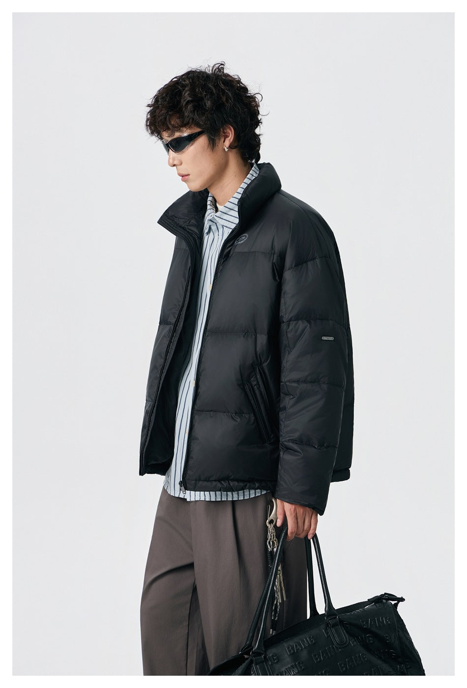 Side view of a model wearing an unzipped black padded jacket with a high collar and zip pockets.
