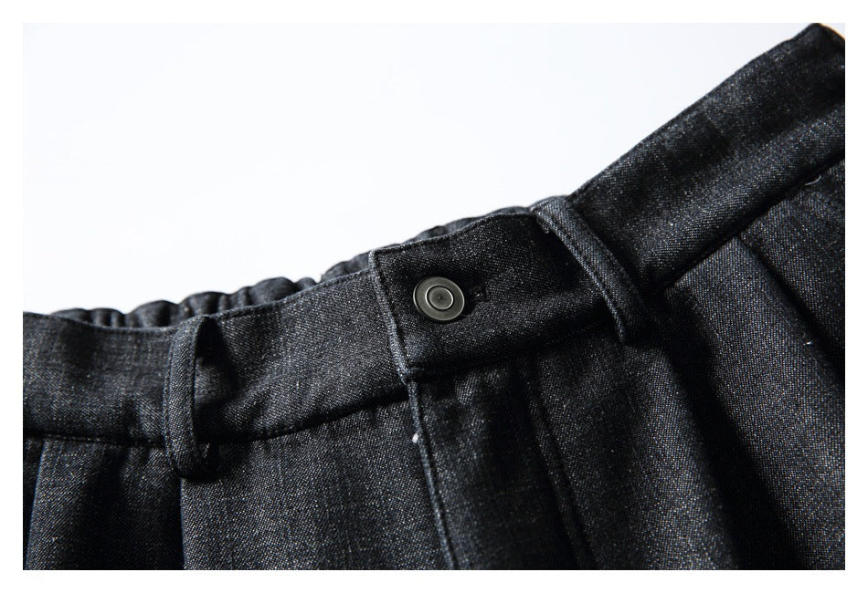 Close-up of charcoal-black trouser waistband, button, belt loop and front pleats.