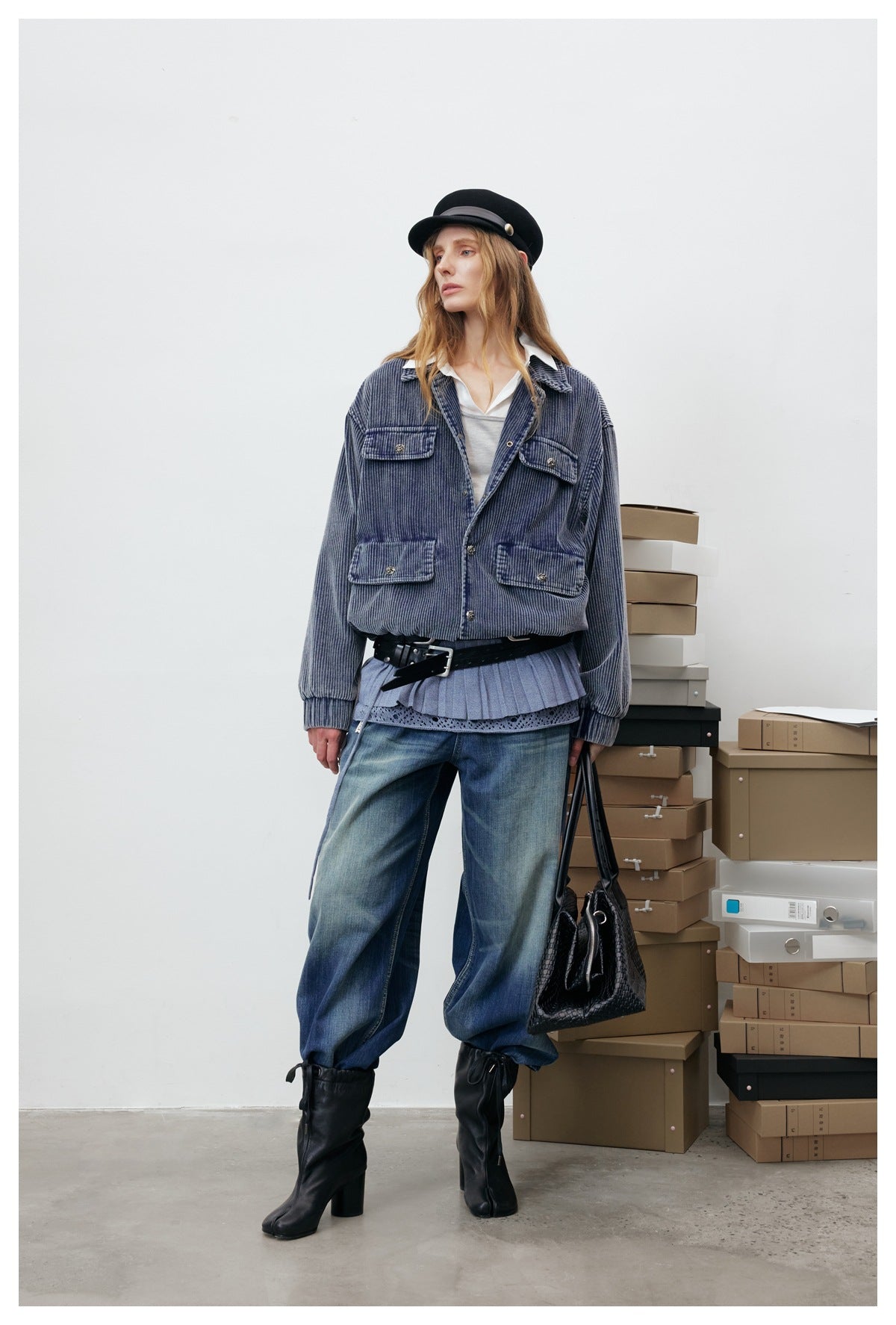 Model wearing the blue corduroy jacket open over a white top, with wide jeans, black boots, cap and bag