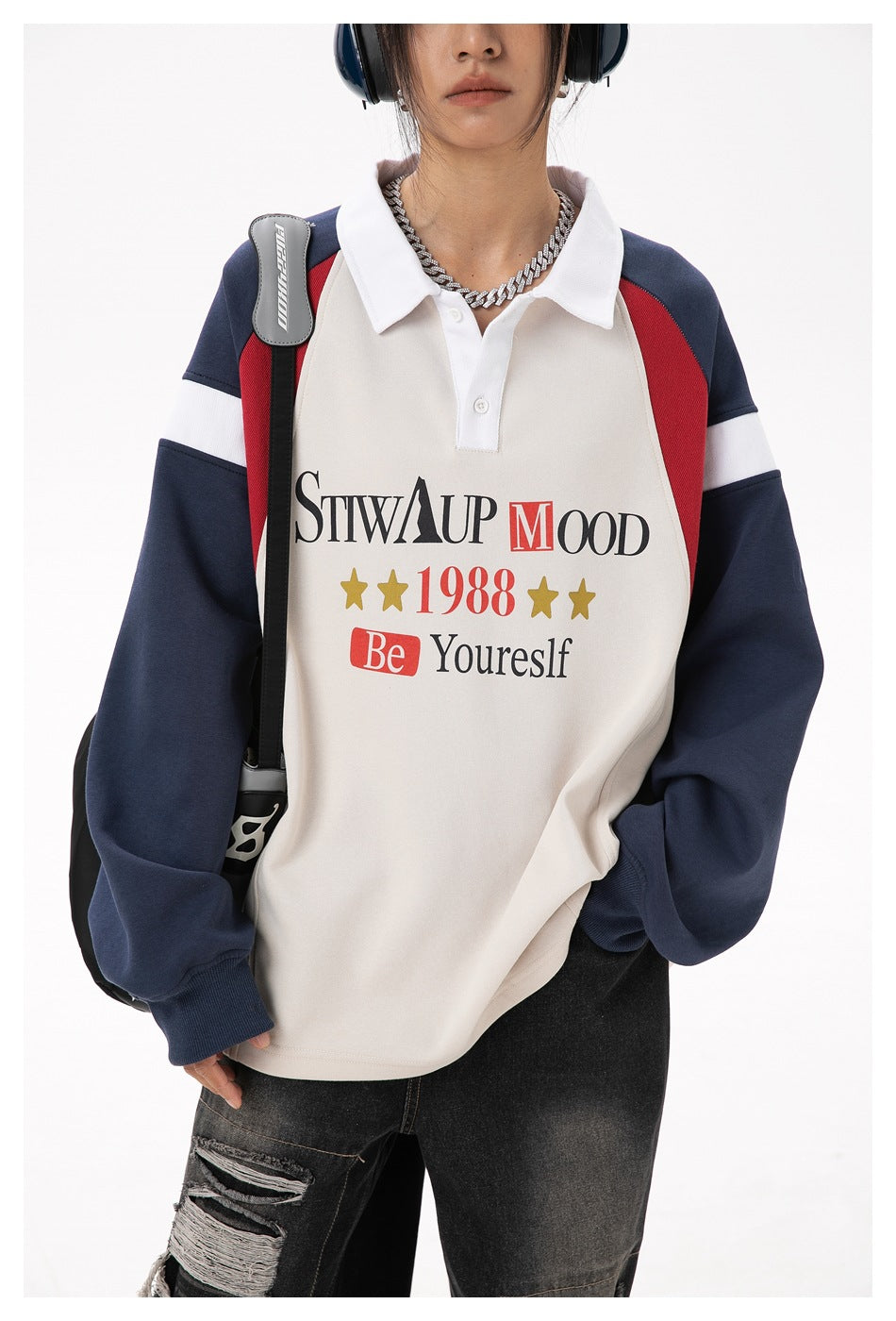 Close view of a model wearing a cream polo-style top with navy sleeves, red panels, white stripes, and bold text and stars.