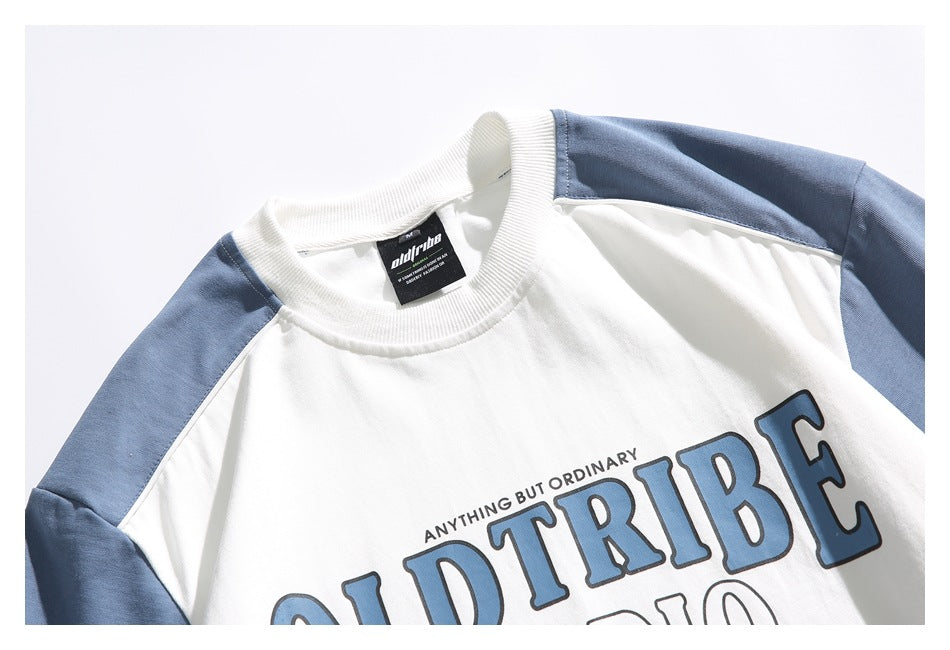 Cropped front view of a white crewneck shirt with blue raglan sleeves and large blue outlined chest lettering.
