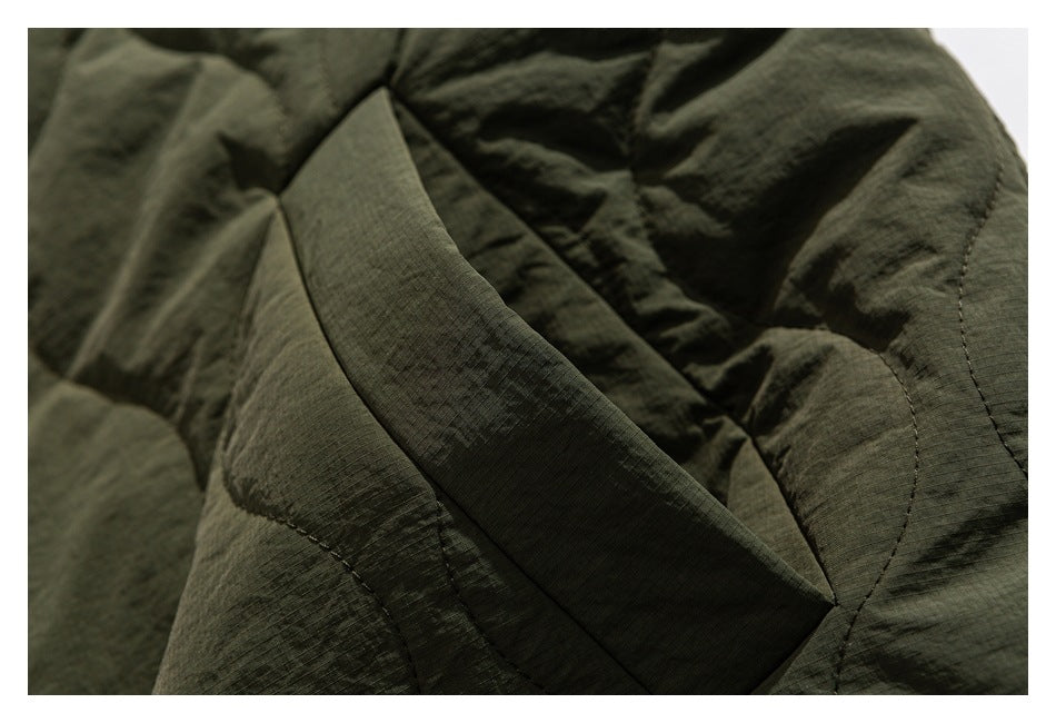Close-up of an olive-green jacket showing a slanted pocket opening and quilted panels.
