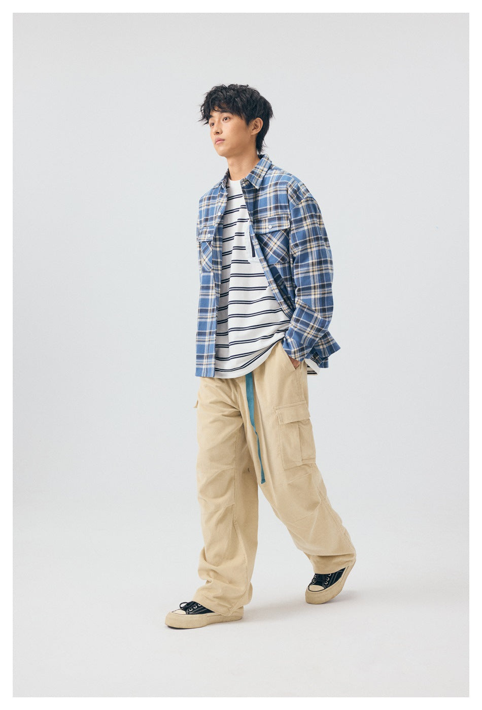 Three-quarter view of a model wearing a blue plaid overshirt, striped tee, and beige cargo pants.