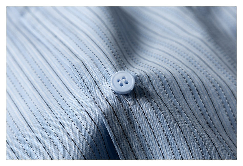Close-up of a pale button on the light blue striped shirt fabric.