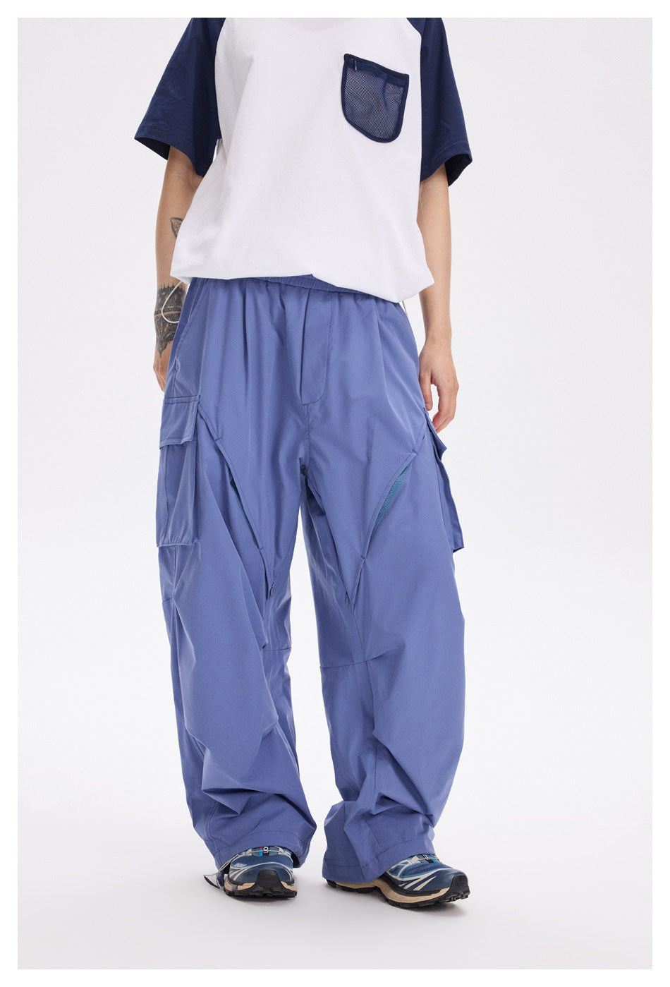 Front view of a model wearing loose periwinkle cargo pants with cargo pockets and angled zip details.