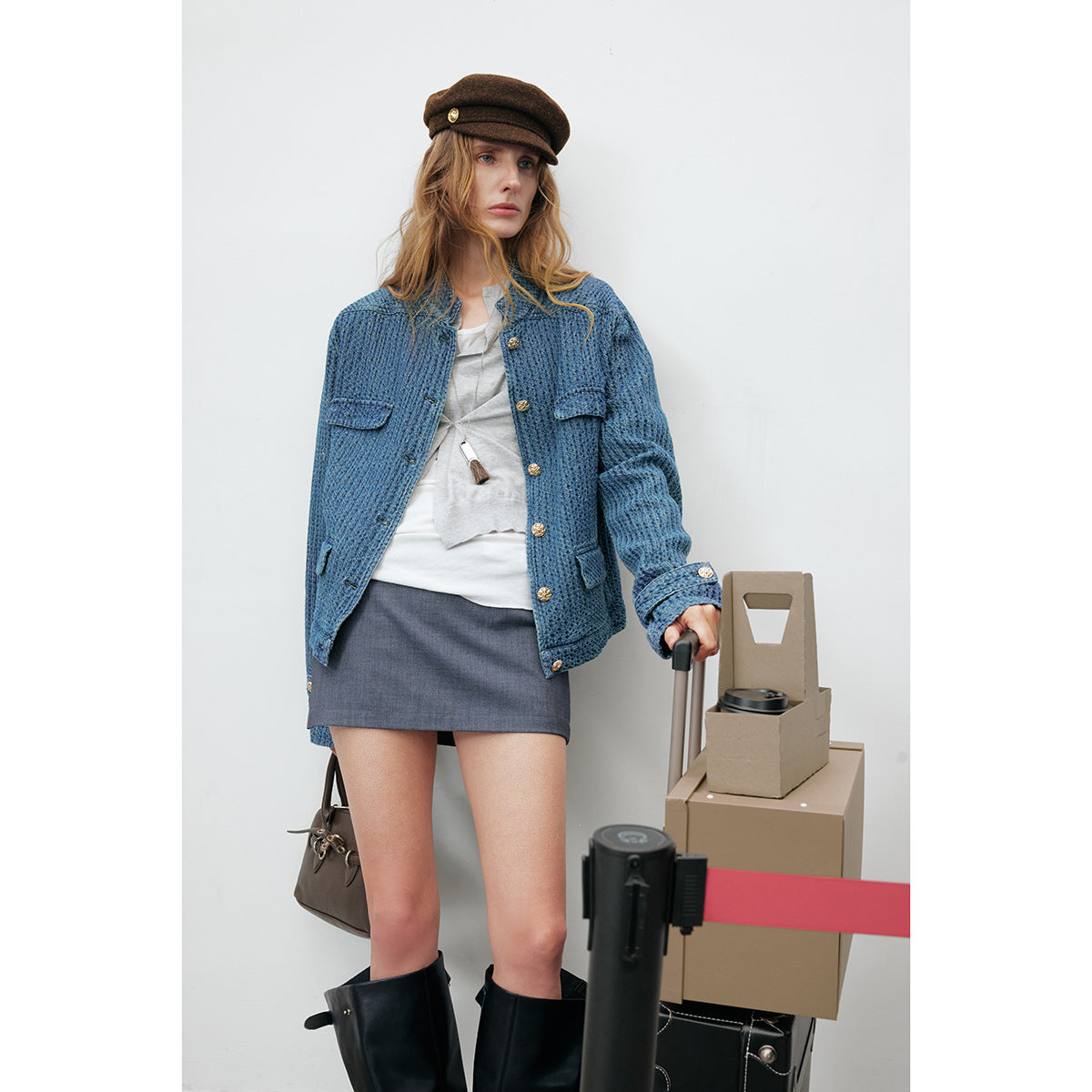 Model wearing an open blue textured jacket with gold buttons, a white top, and a gray mini skirt.