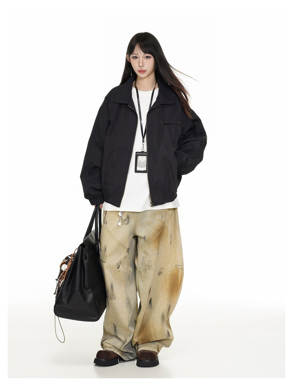 Model wearing a black collared zip jacket open over a white tee and wide-leg pants, holding a black tote bag