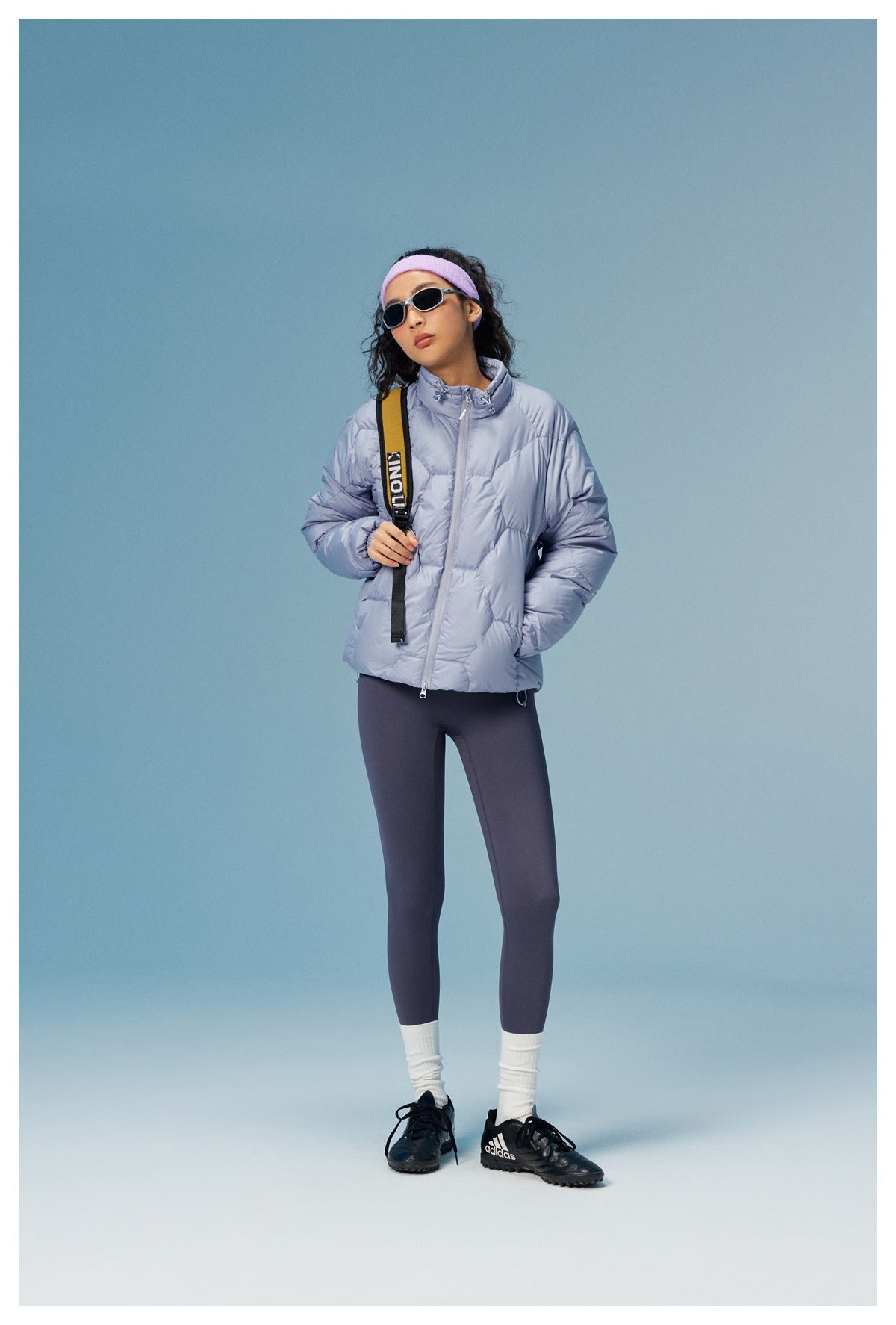 Full-length model wearing a lavender-gray quilted jacket with a high collar, paired with dark leggings.