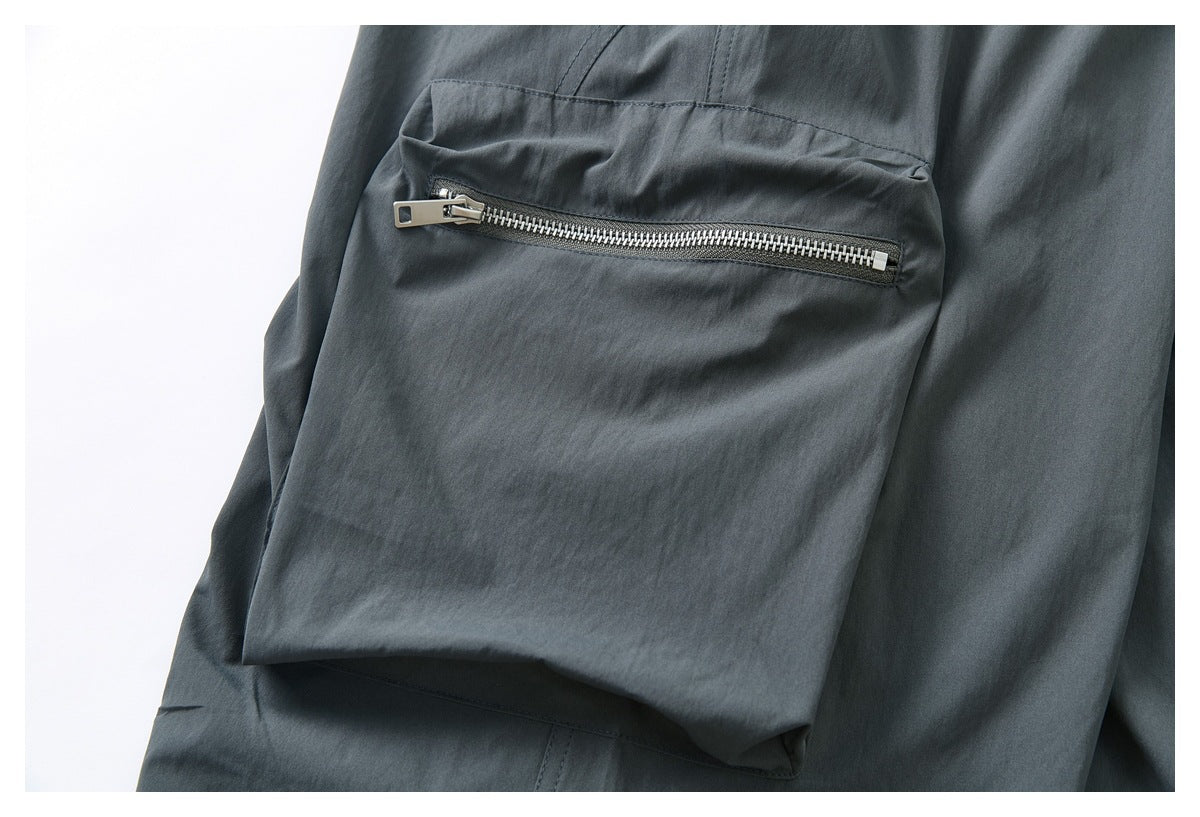 Close-up of charcoal-gray trousers showing a flap pocket with a horizontal silver zipper.