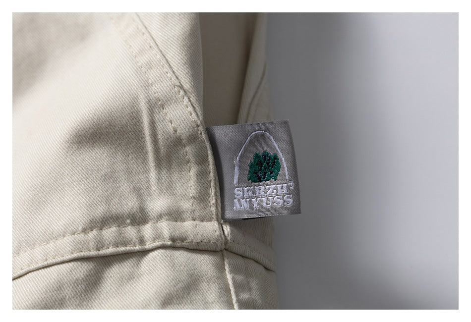 Close-up of a small embroidered label sewn into the seam of light beige shorts.