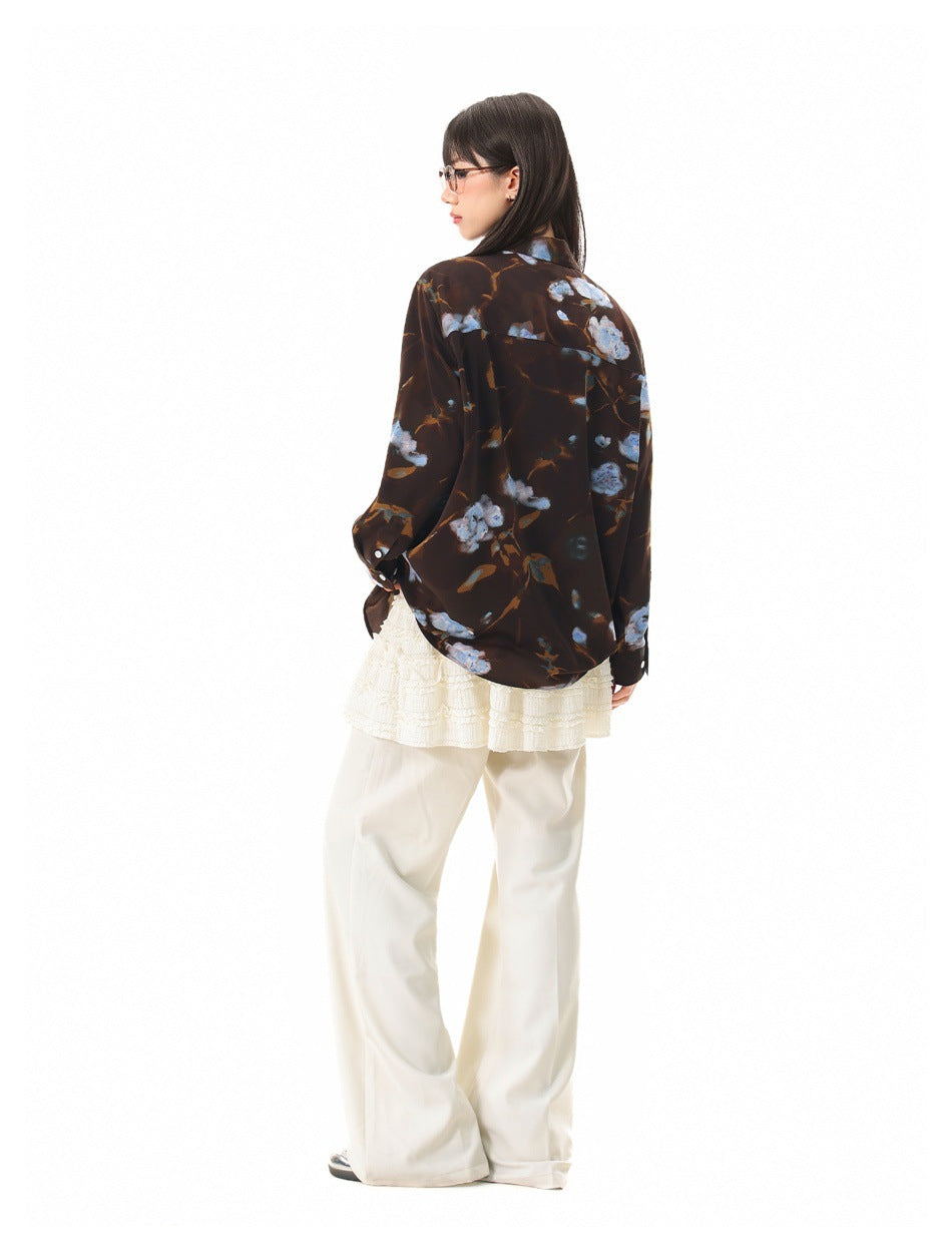 Model wearing a dark brown floral button-up shirt, shown from behind with an ivory skirt and wide-leg trousers.
