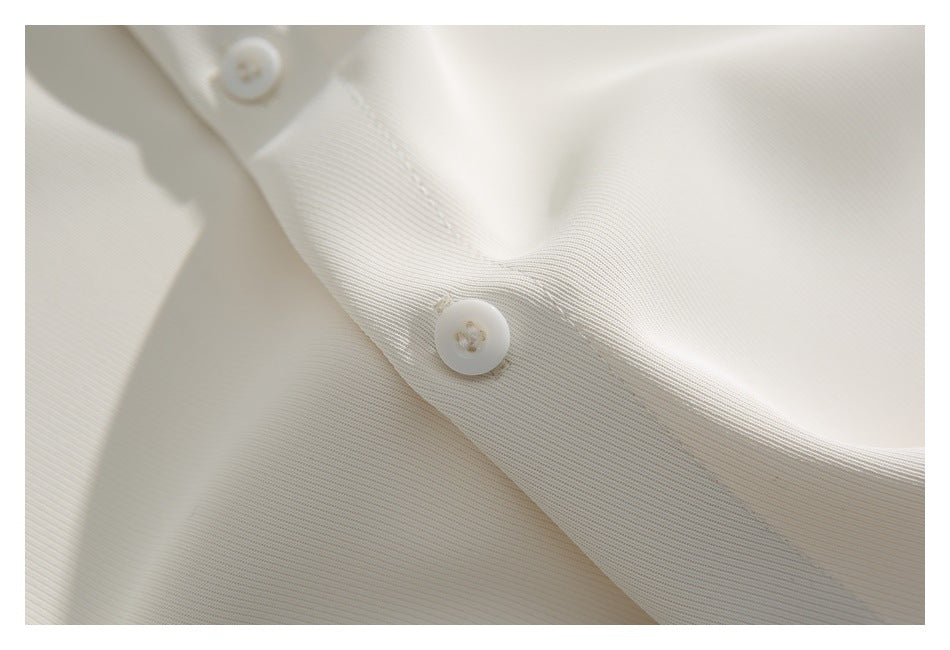 Close-up of a white button and buttonhole on the ivory shirt placket.