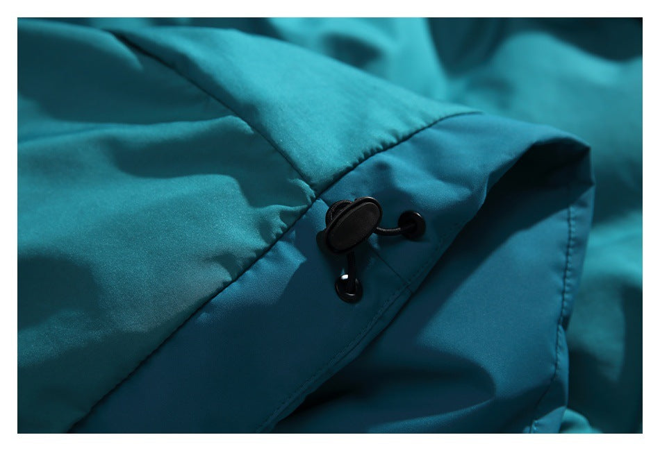Close-up of a black drawcord toggle on teal jacket fabric.