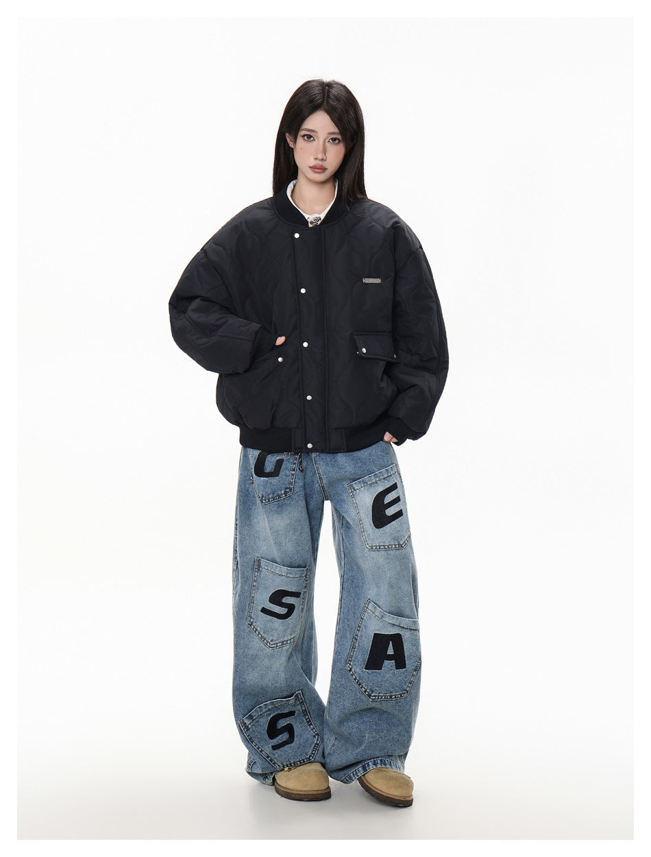 Woman wearing an oversized black quilted bomber jacket with snap front over wide-leg jeans with letter patches
