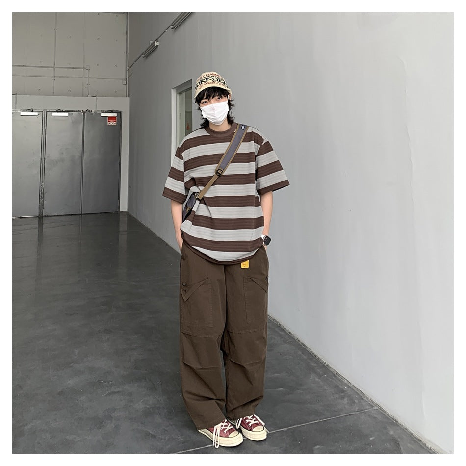 Person wearing a brown and gray striped T-shirt with loose brown cargo pants, a cap, and a crossbody bag.