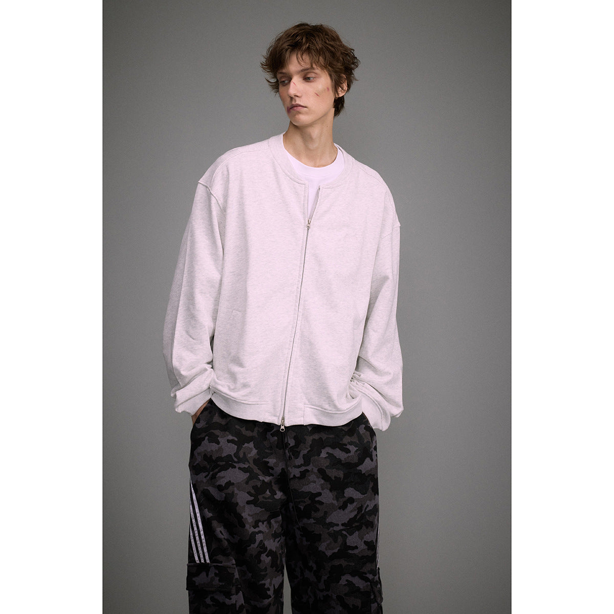 Model wearing a light gray zip-front sweatshirt with oversized dark camouflage cargo trousers.
