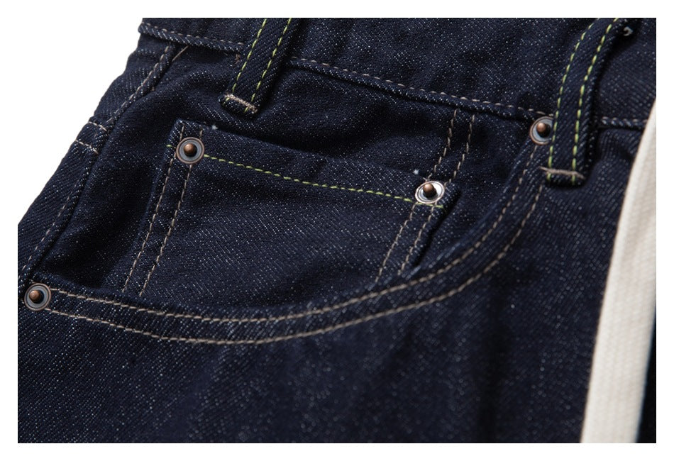 Close-up of the small riveted coin pocket and front pocket on dark indigo jeans with contrast stitching.