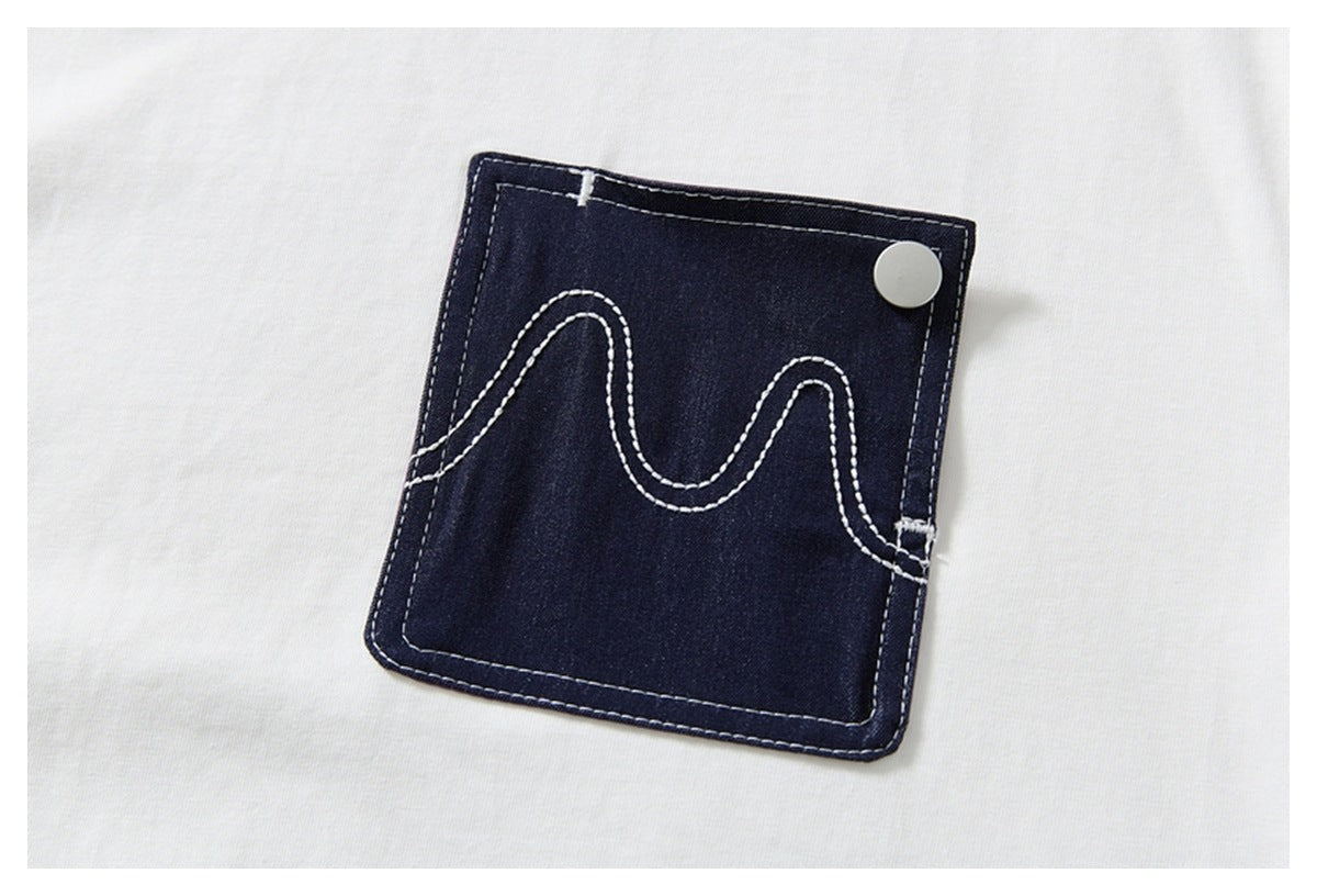 Close-up of a dark indigo patch pocket with white wavy stitching and a silver button on a white shirt.