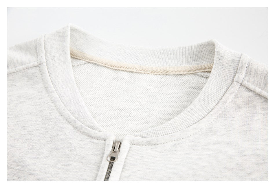 Close-up of a light gray sweatshirt's ribbed crew neck, inner seam tape, and front zipper.