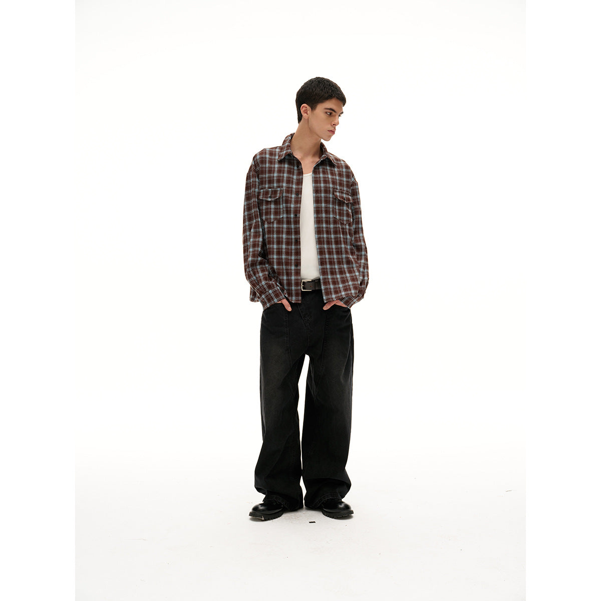 Full-length model wearing a brown plaid button-up shirt over a white tee with loose black trousers.