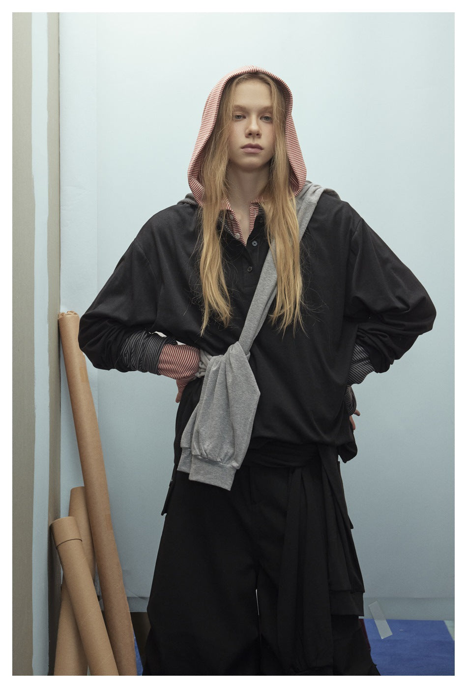 Front view of a model wearing a black hooded top with red striped hood and cuffs, gray layer, and black bottoms.