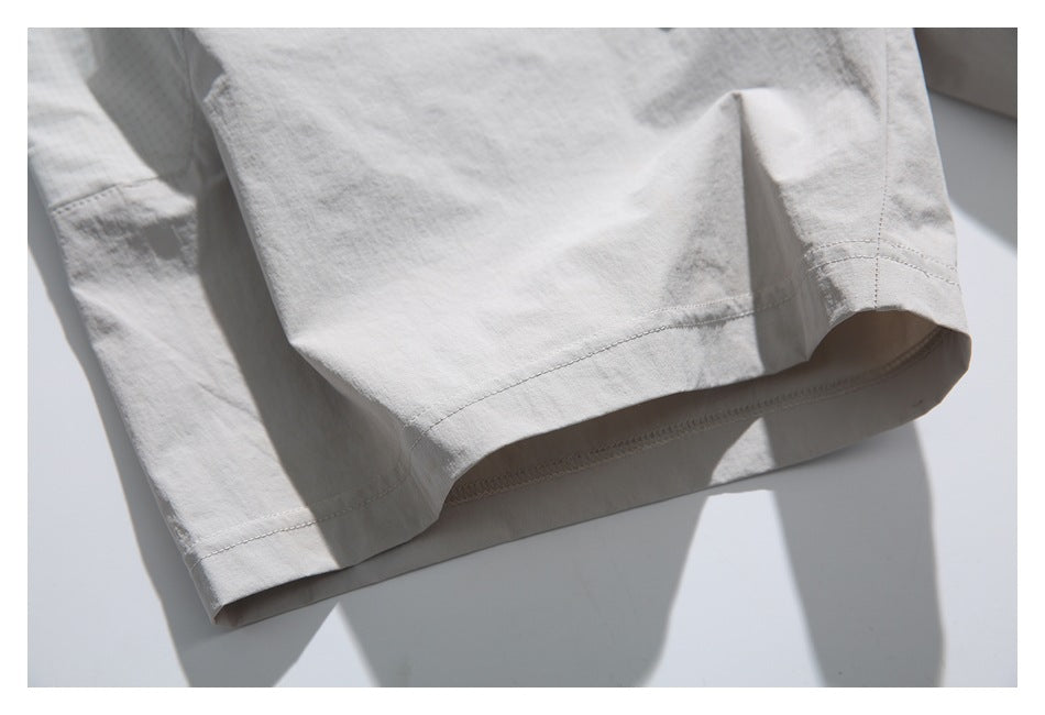 Close-up of the stitched lower hem and side seam on light gray shorts.