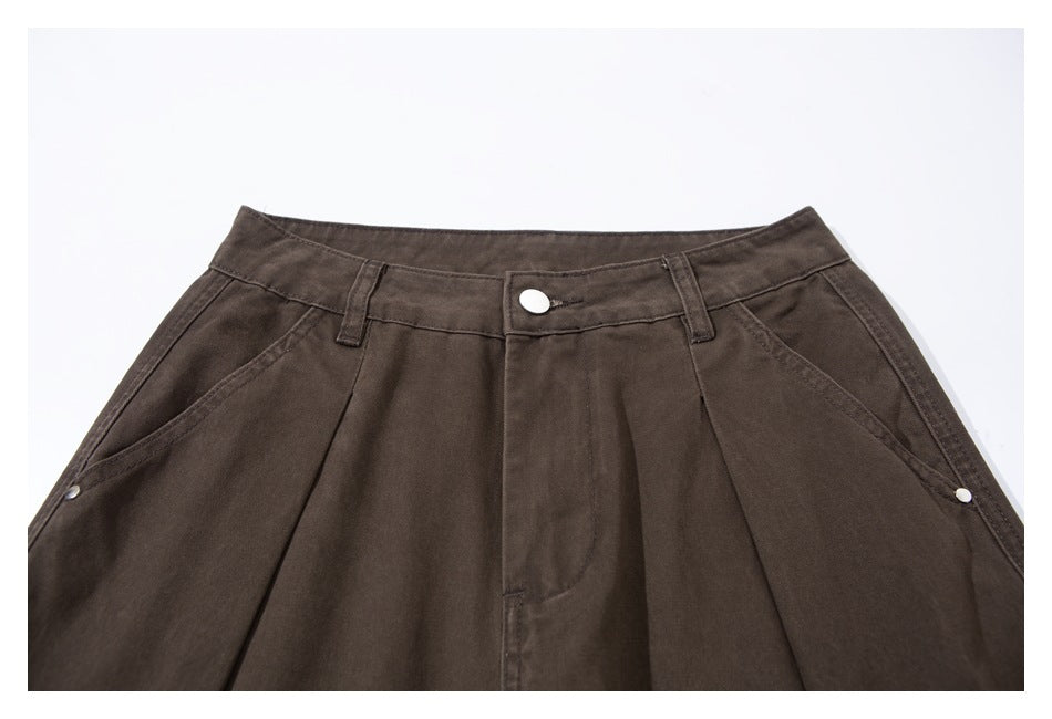 Close-up of dark brown pants’ front waistband, button, belt loops, pleats and angled pockets.