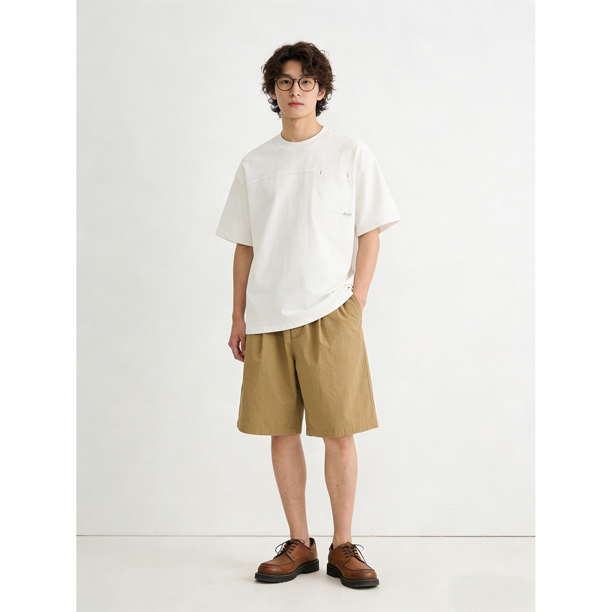 Model wearing a white short-sleeve T-shirt with a chest pocket and tan shorts.