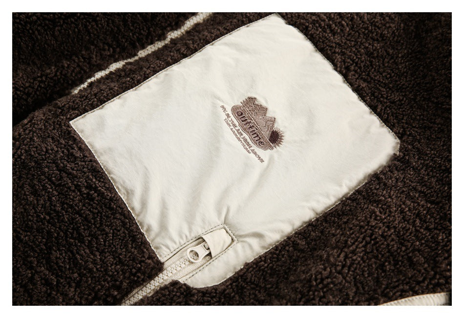 Close-up of a cream garment panel with embroidered lettering and a cream zipper against dark brown fleece.