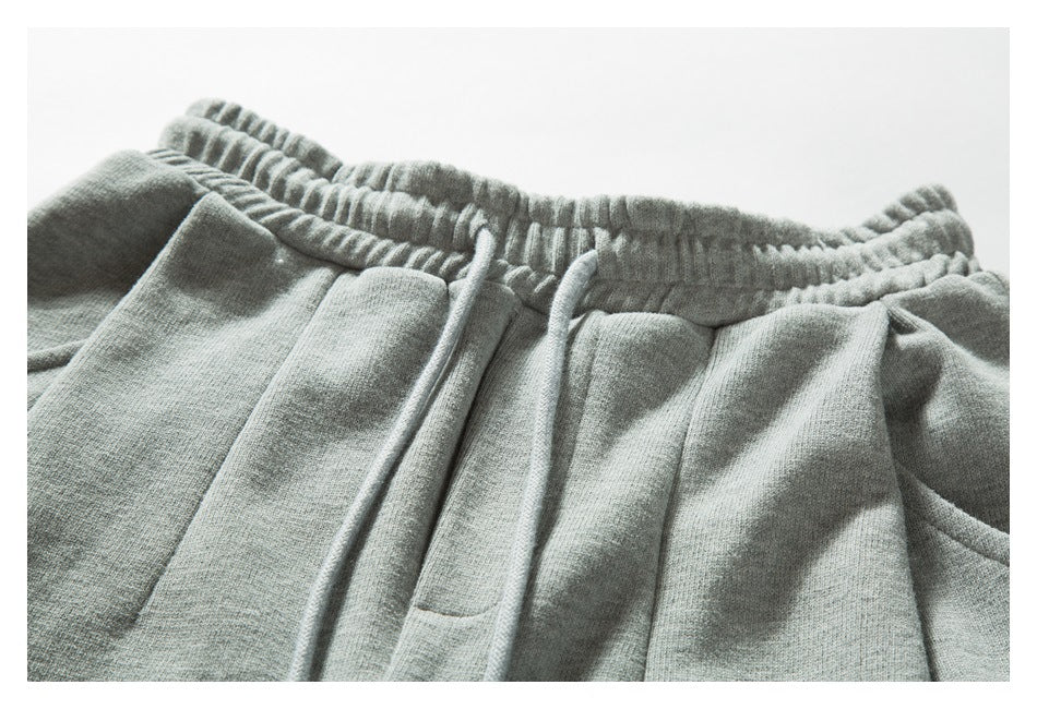 Close-up of light gray sweatpants showing the gathered elastic waistband, matching drawstrings and front pleats.