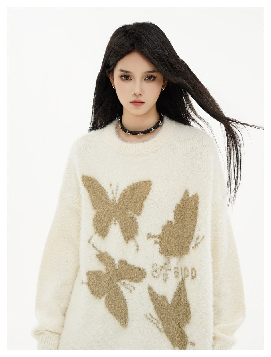 Close view of an ivory sweater with tan butterfly motifs and a crew neckline, worn by a model.