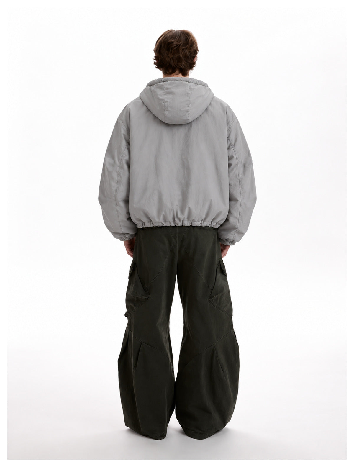 Back view of a model in a light gray hooded jacket with a drawstring hem and wide dark olive cargo pants