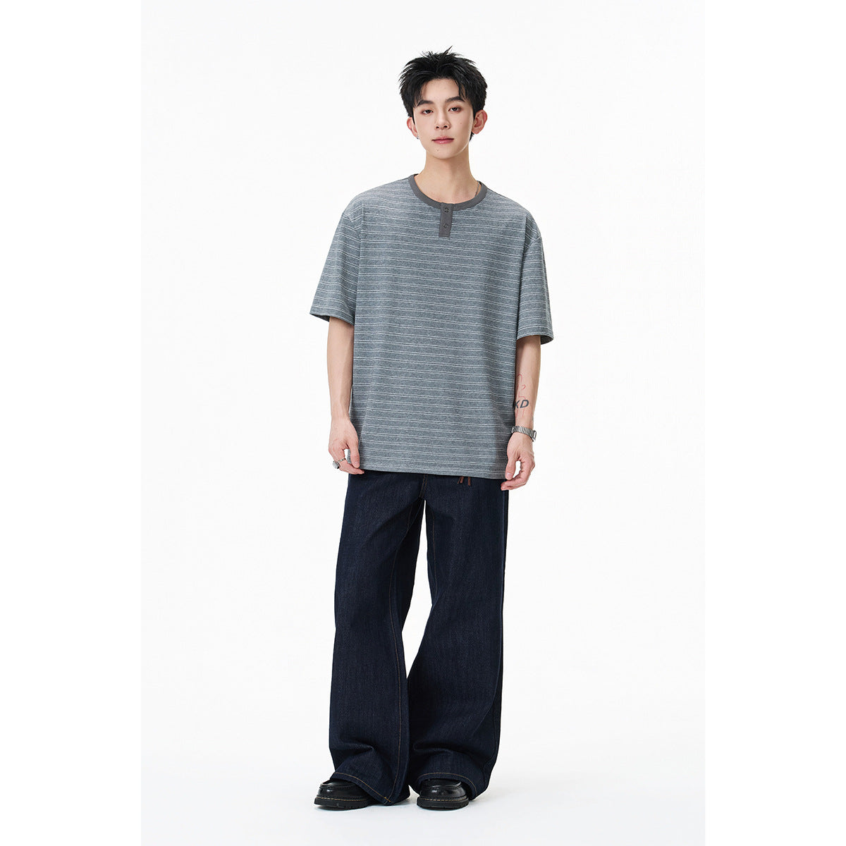 Model wearing an oversized gray striped short-sleeve Henley with dark jeans.