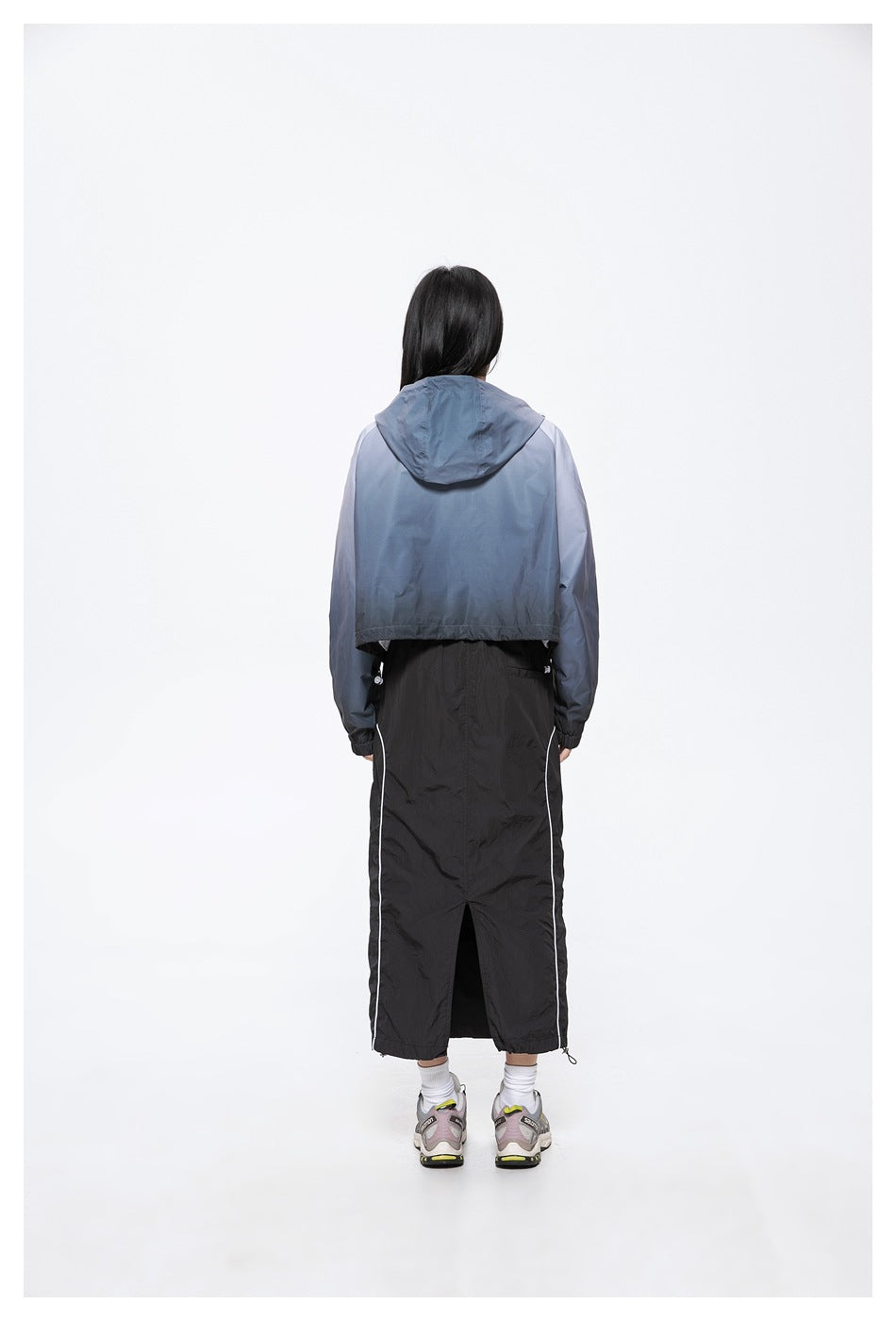 Back view of a model wearing a blue-gray hooded jacket over a long black skirt with white side piping.