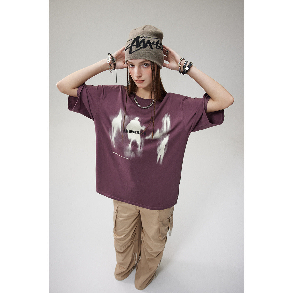 Model wearing an oversized plum graphic T-shirt with beige cargo pants and a taupe beanie.