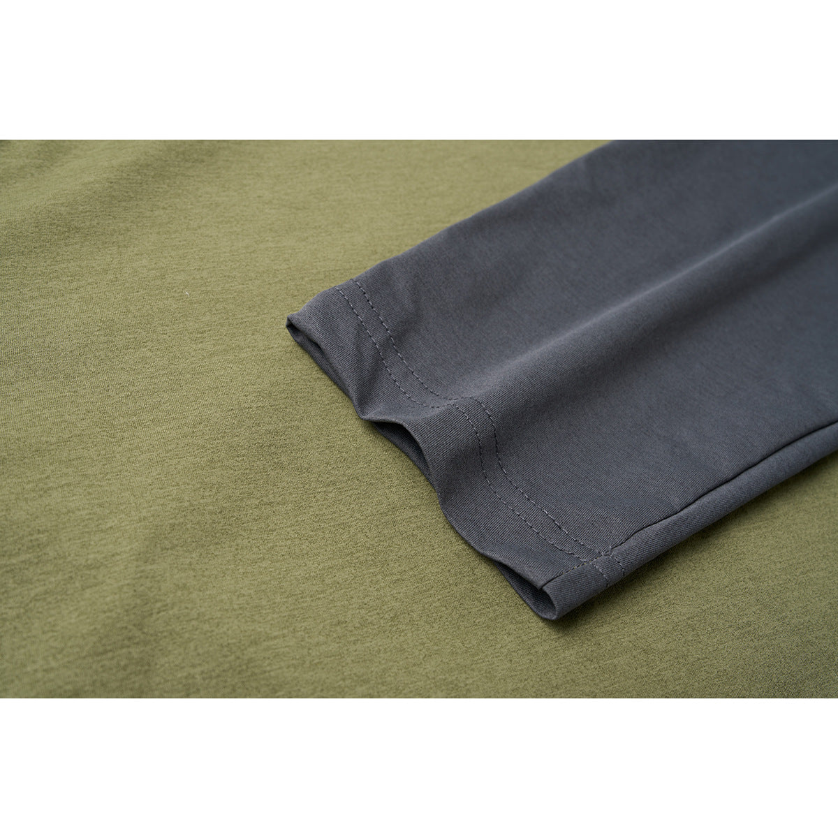 Close-up of a charcoal-gray sleeve and stitched cuff against the olive-green body of a shirt.