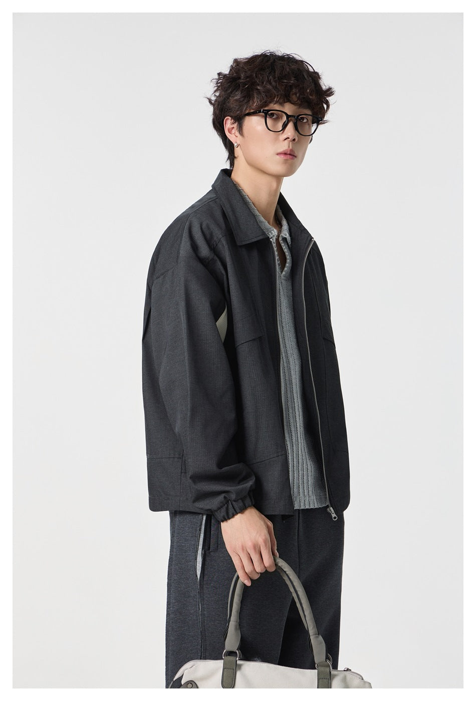 Closer angled view of a model wearing a charcoal zip-front jacket with a pointed collar and flap chest pockets.