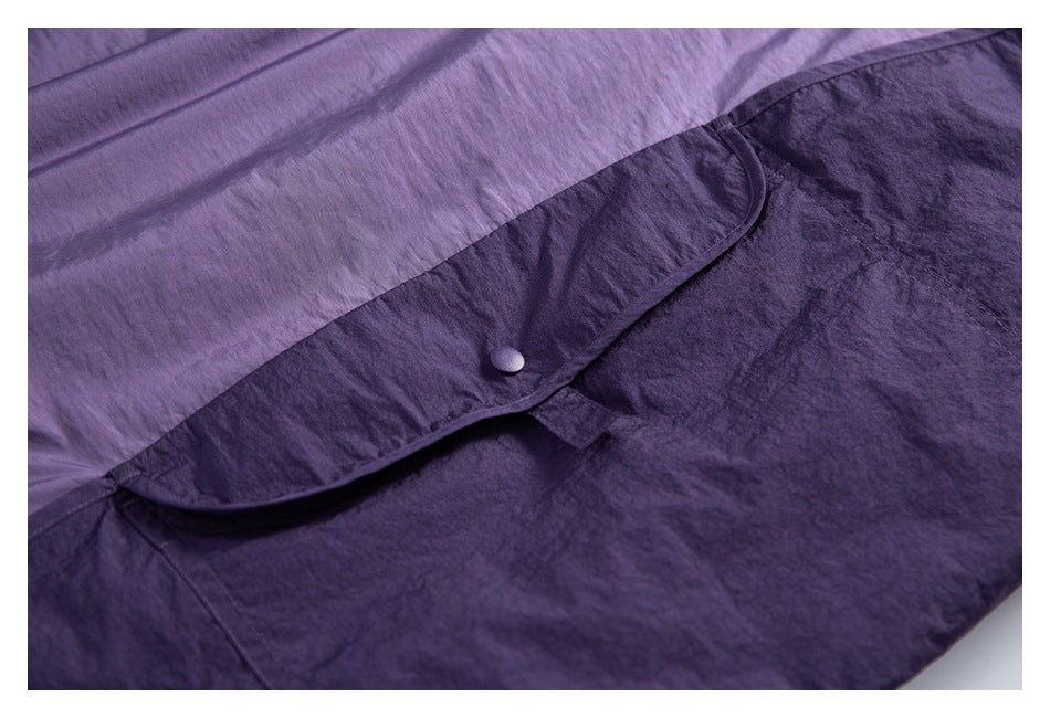 Close-up of a dark purple garment showing a curved flap with a matching snap button and stitched seams.