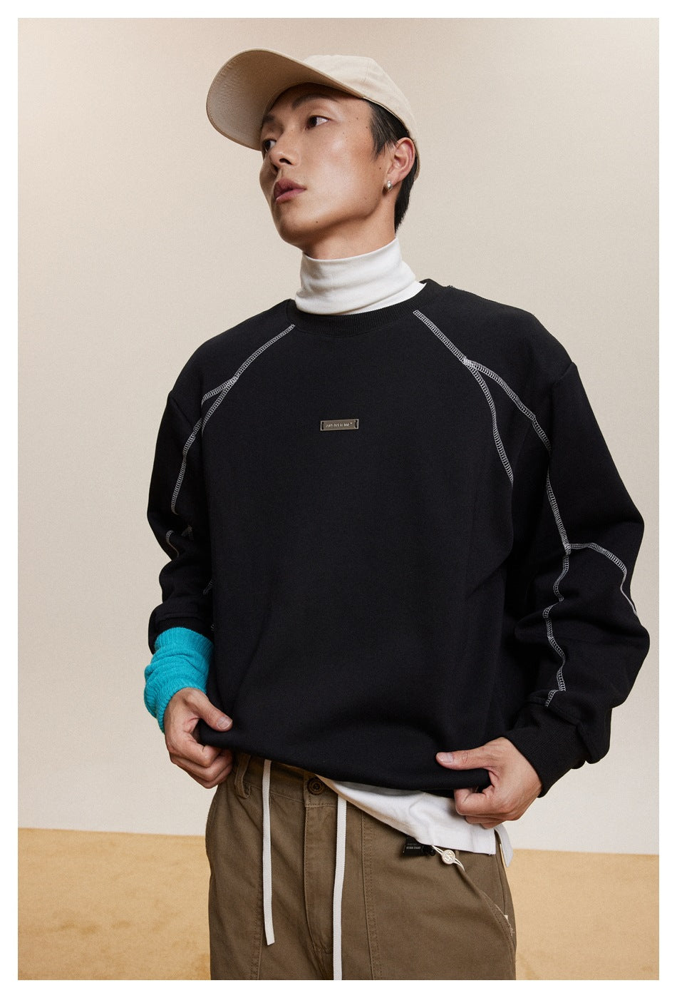 Front view of a model wearing a black crewneck sweatshirt with white contrast seams and a small chest plaque.