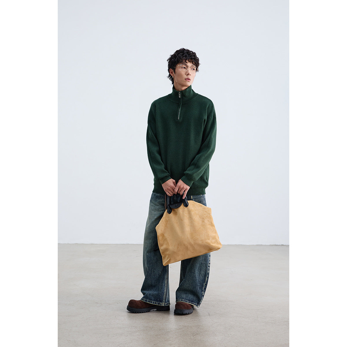 Model wearing a dark green pullover with a high stand collar and short zipper, styled with jeans and a tan bag.