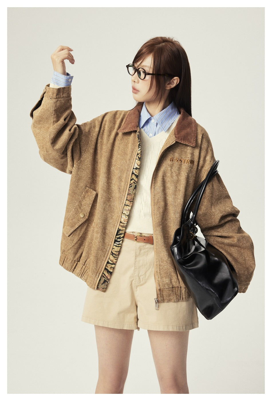 Model wearing an open tan jacket with a brown collar over a cream sweater and beige shorts.