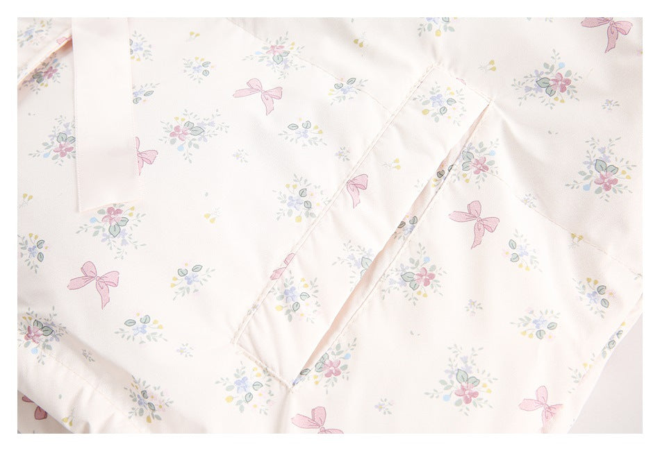 Close-up of pale ivory fabric printed with pastel flowers and pink bows, showing overlapping panels and a seam.